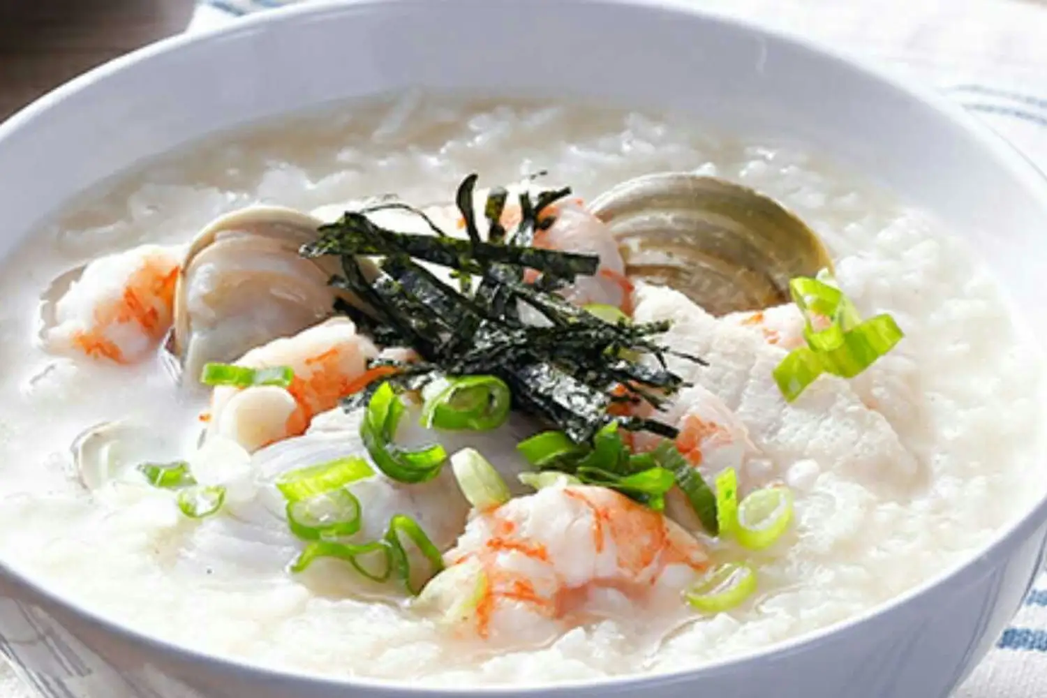 A steaming bowl of Ann's seafood congee topped with green onion and shrimp